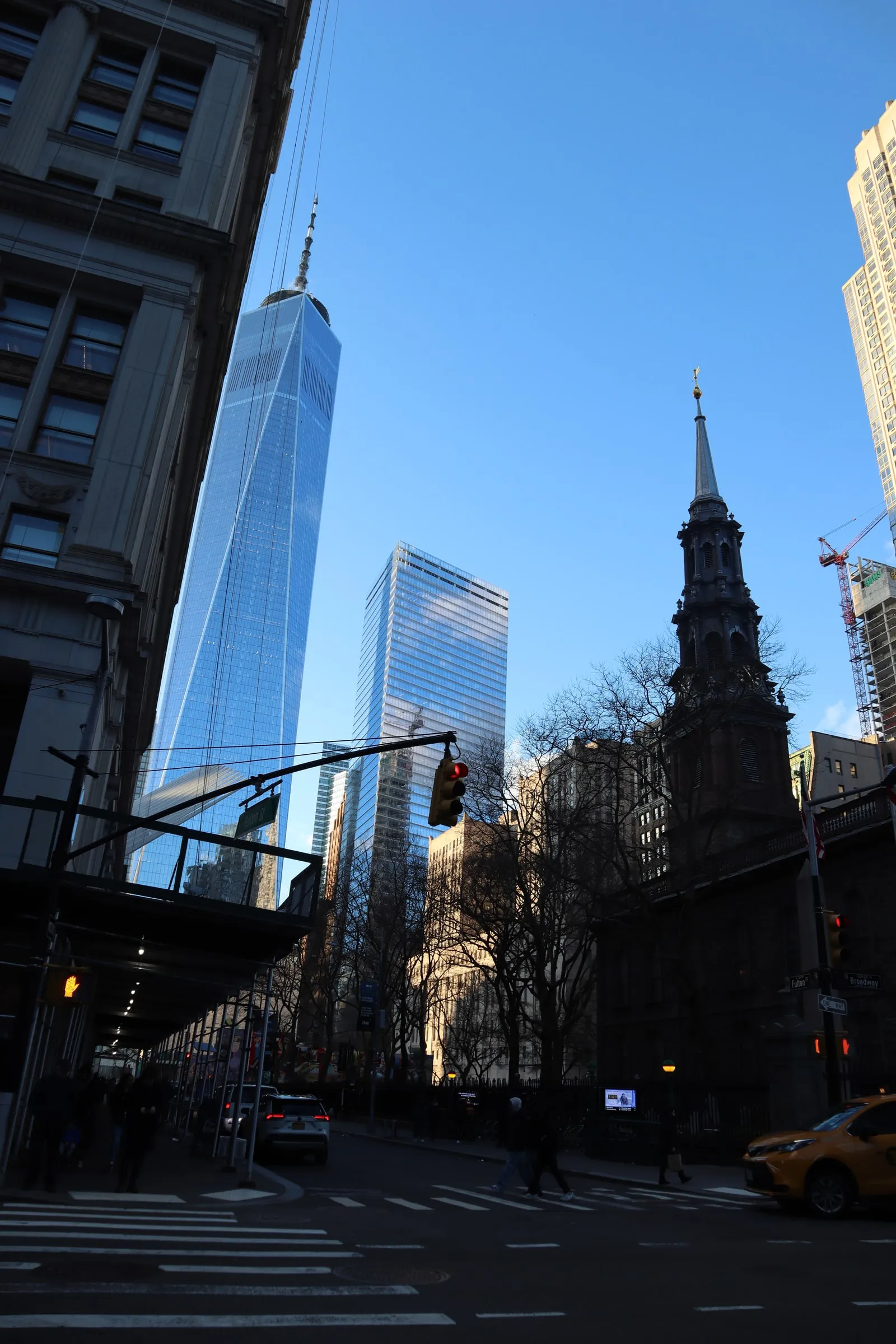 One World Trade Center rising above a church steeple and a street corner.