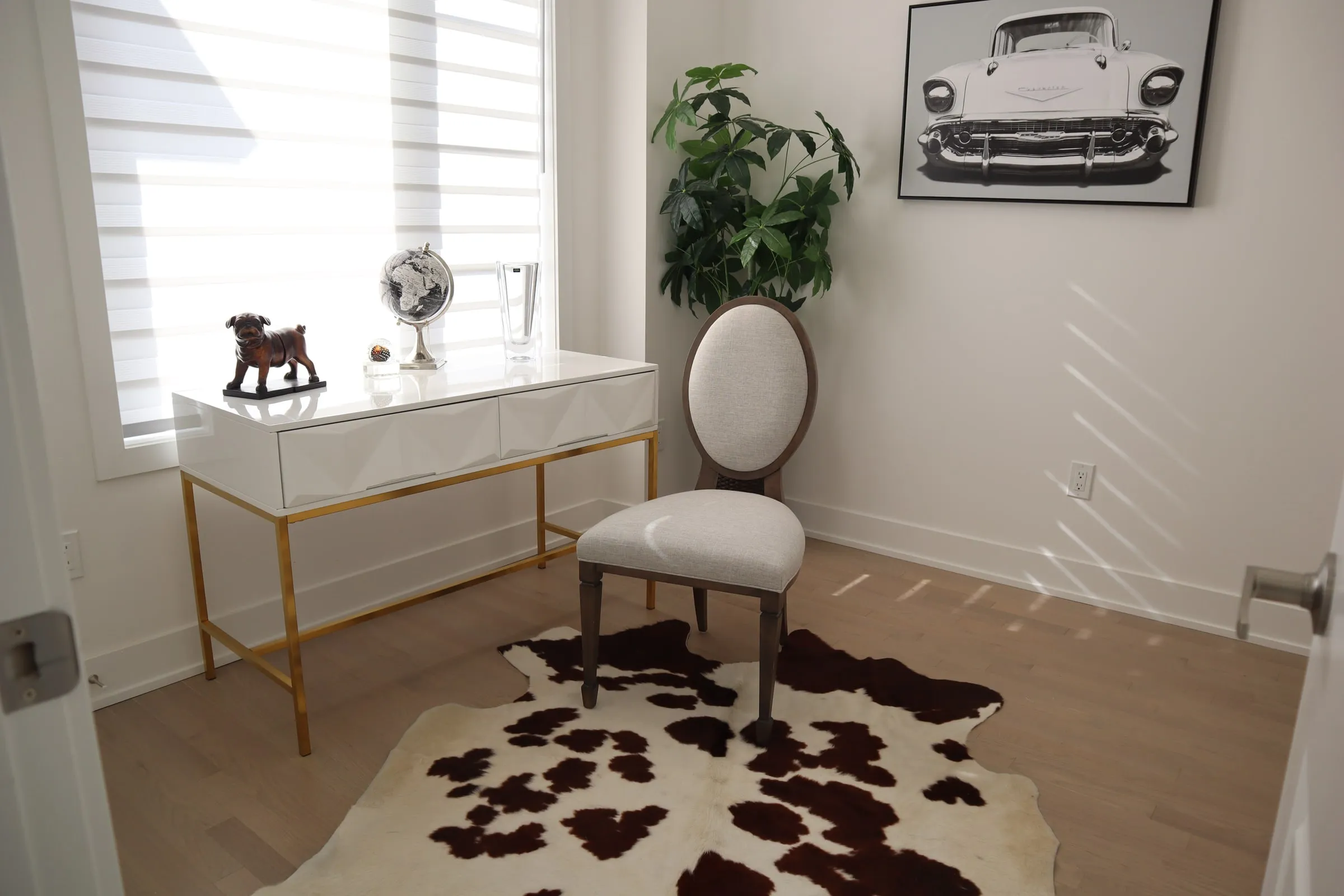 A bright staged room with a white desk, a plant and a cowhide rug.