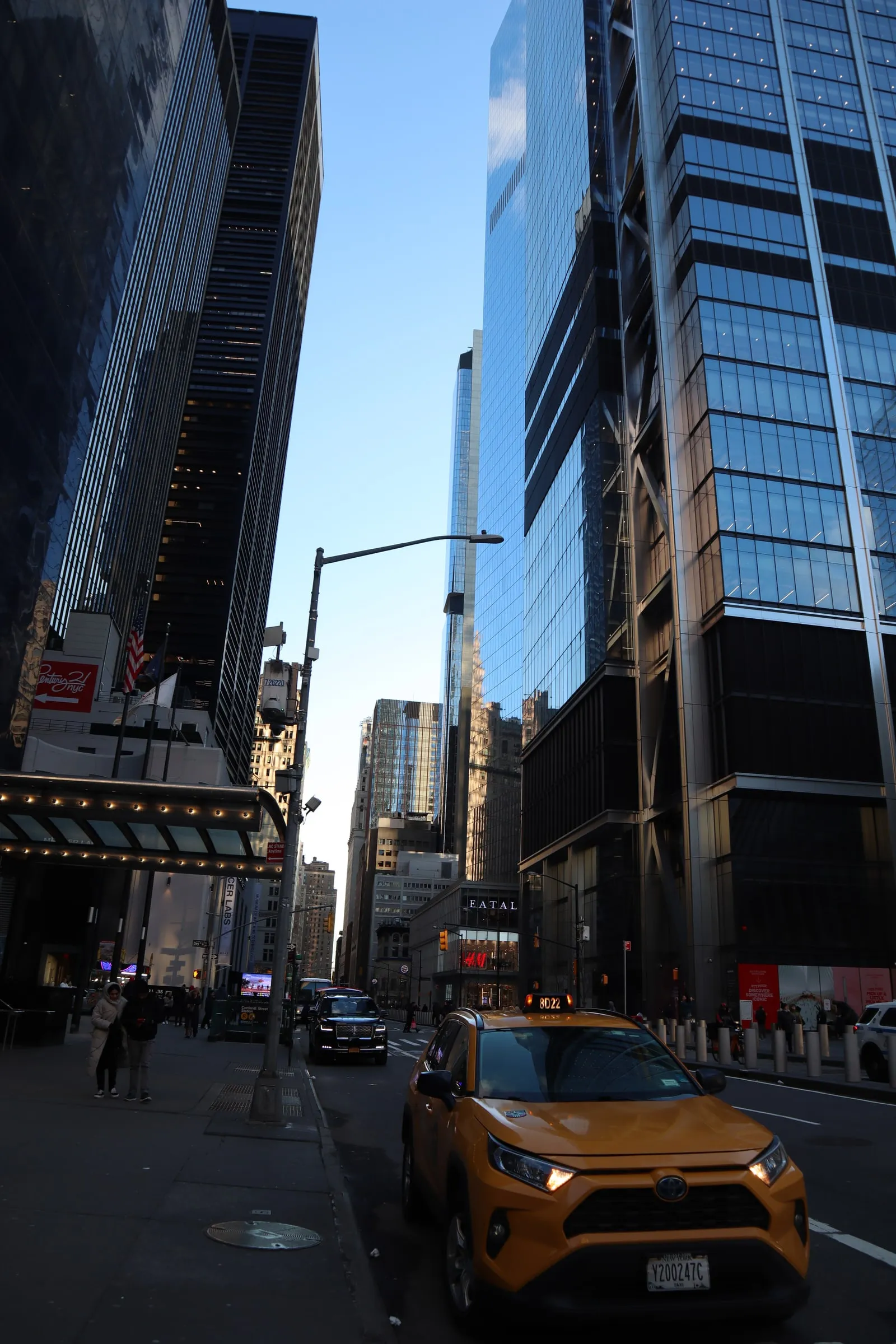 A yellow taxi on a city street between glass towers.